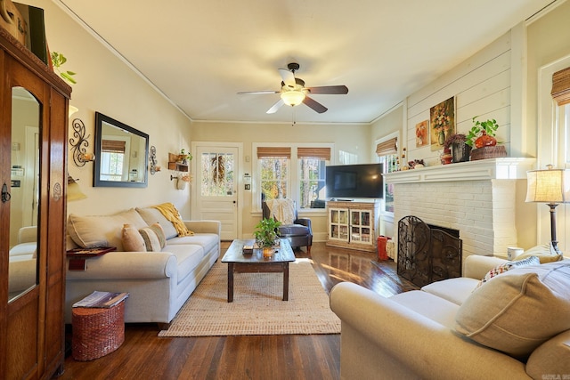 living room featuring ceiling fan, dark hardwood / wood-style flooring, crown molding, and a brick fireplace