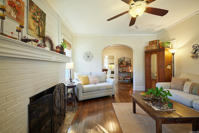 living room featuring a fireplace, ceiling fan, ornamental molding, and dark wood-type flooring