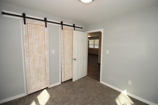 unfurnished bedroom with dark carpet and a barn door