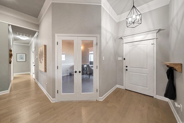 foyer entrance featuring an inviting chandelier, light wood-type flooring, ornamental molding, and french doors