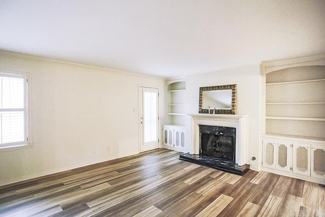 unfurnished living room featuring built in shelves, dark hardwood / wood-style floors, and crown molding