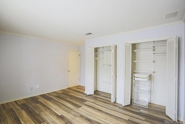 unfurnished bedroom with dark hardwood / wood-style flooring, two closets, and ornamental molding