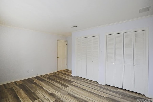 unfurnished bedroom with dark wood-type flooring, two closets, and ornamental molding