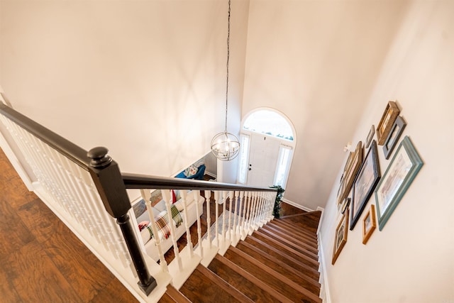 stairs featuring wood-type flooring, a high ceiling, and an inviting chandelier