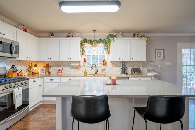 kitchen featuring white cabinetry, sink, stainless steel appliances, pendant lighting, and ornamental molding