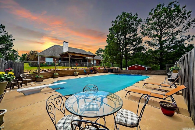 pool at dusk featuring a patio and a diving board