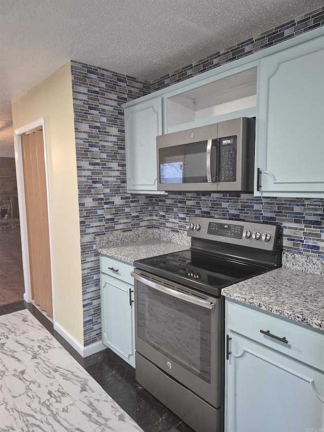 kitchen featuring light stone countertops, appliances with stainless steel finishes, tasteful backsplash, a textured ceiling, and white cabinets