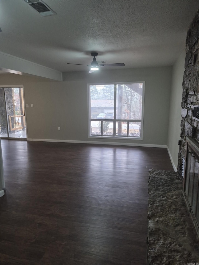 empty room featuring dark hardwood / wood-style flooring, ceiling fan, a fireplace, and a textured ceiling