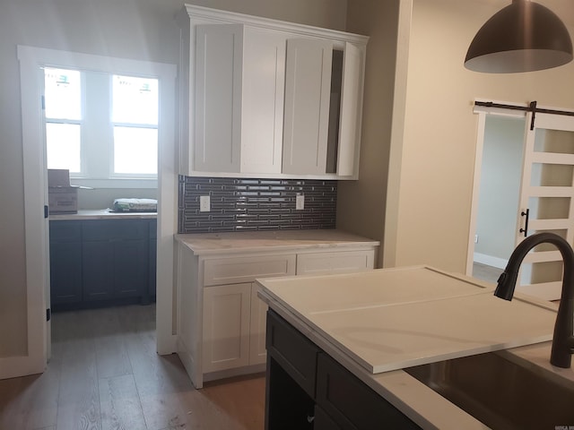 kitchen featuring sink, a barn door, light hardwood / wood-style flooring, backsplash, and white cabinets