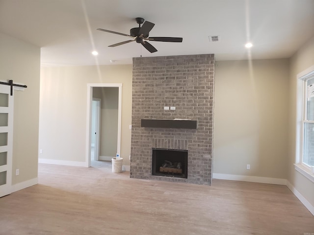 unfurnished living room featuring a barn door, light hardwood / wood-style flooring, a brick fireplace, and ceiling fan