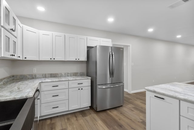 kitchen featuring stainless steel fridge, light stone countertops, and white cabinetry