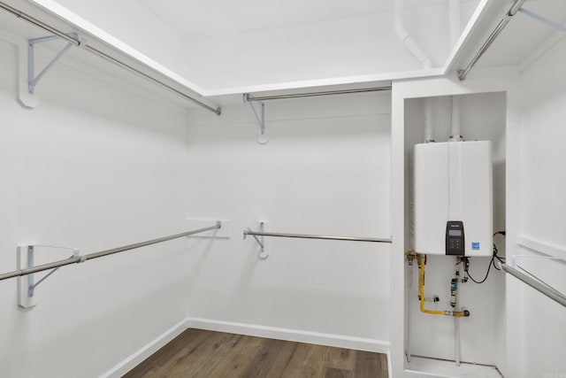 spacious closet featuring tankless water heater and dark wood-type flooring