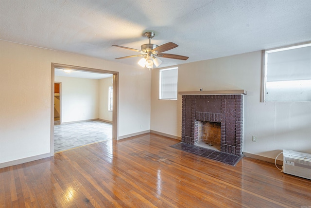 unfurnished living room featuring ceiling fan, a fireplace, wood-type flooring, and a textured ceiling