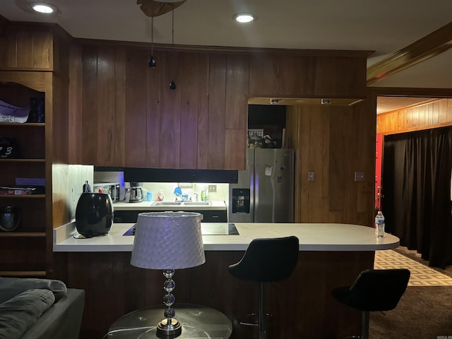 kitchen featuring a kitchen bar, stainless steel fridge, kitchen peninsula, and wooden walls