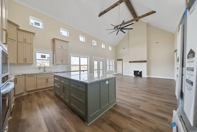 kitchen with a center island, sink, light stone countertops, tasteful backsplash, and beamed ceiling