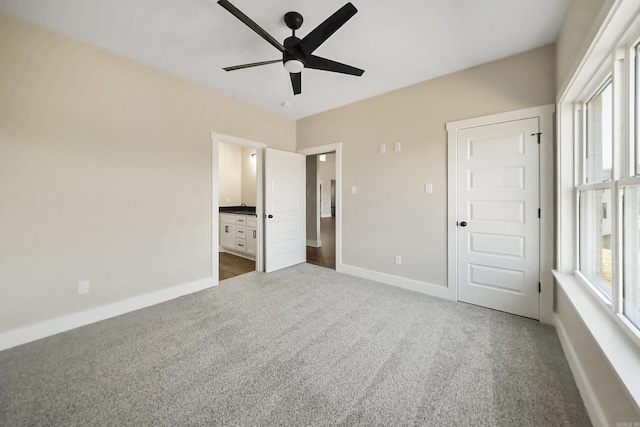 unfurnished bedroom featuring ensuite bath, ceiling fan, and dark colored carpet