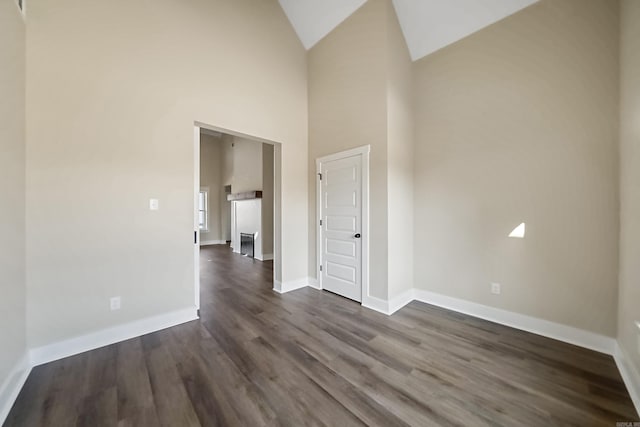 unfurnished room with high vaulted ceiling and dark wood-type flooring