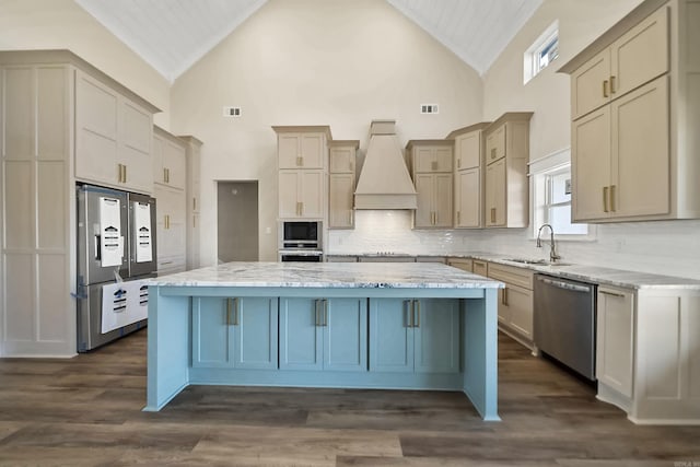 kitchen with stainless steel appliances, light stone counters, backsplash, a kitchen island, and custom exhaust hood