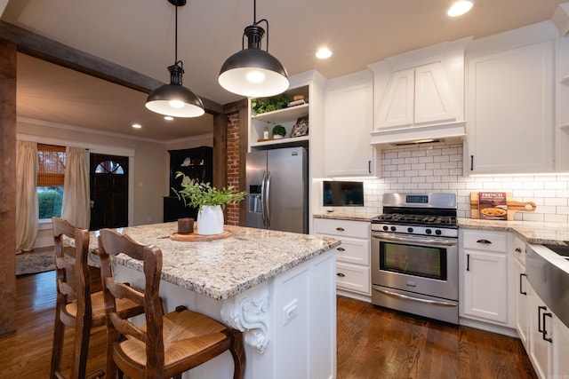 kitchen featuring a center island, light stone countertops, appliances with stainless steel finishes, decorative light fixtures, and white cabinetry