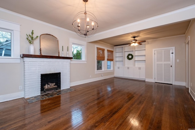 unfurnished living room with dark wood-type flooring, ceiling fan with notable chandelier, built in shelves, ornamental molding, and a fireplace