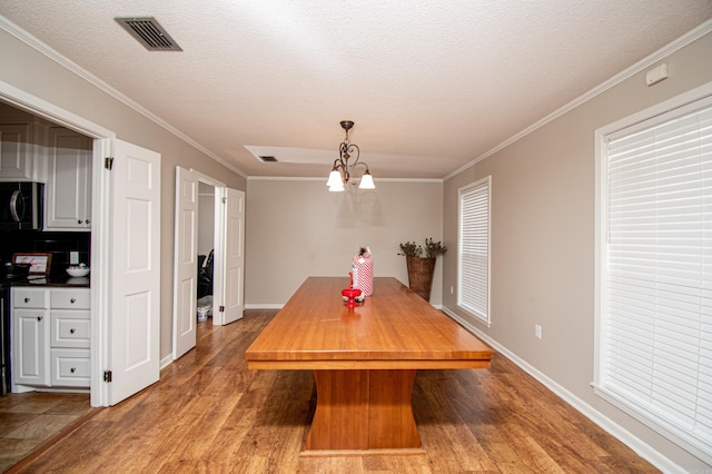 dining space featuring hardwood / wood-style floors, ornamental molding, a textured ceiling, and an inviting chandelier