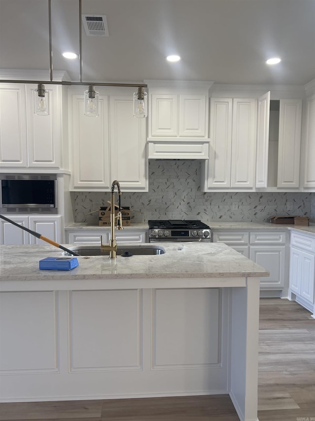 kitchen with white cabinetry, a sink, visible vents, stainless steel appliances, and light stone countertops