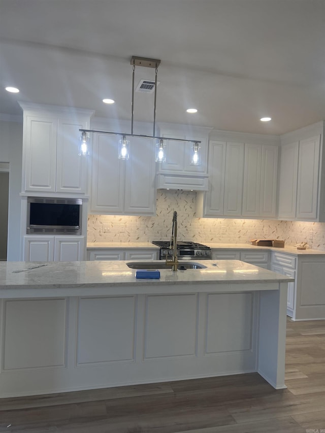 kitchen featuring a sink, tasteful backsplash, visible vents, white cabinetry, and wood finished floors