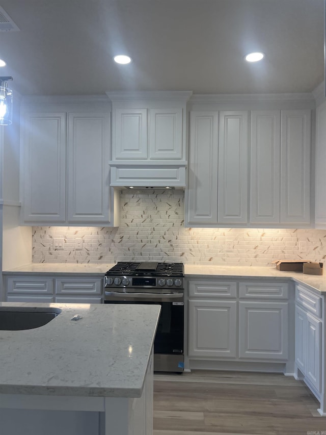 kitchen with white cabinets, stainless steel gas range oven, and decorative backsplash