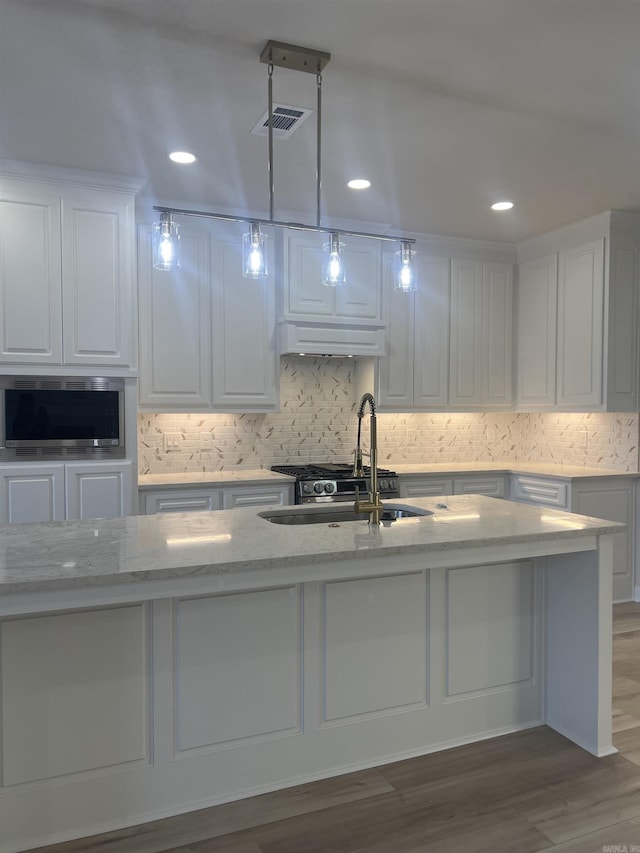 kitchen with white cabinets, a sink, visible vents, light stone countertops, and wood finished floors
