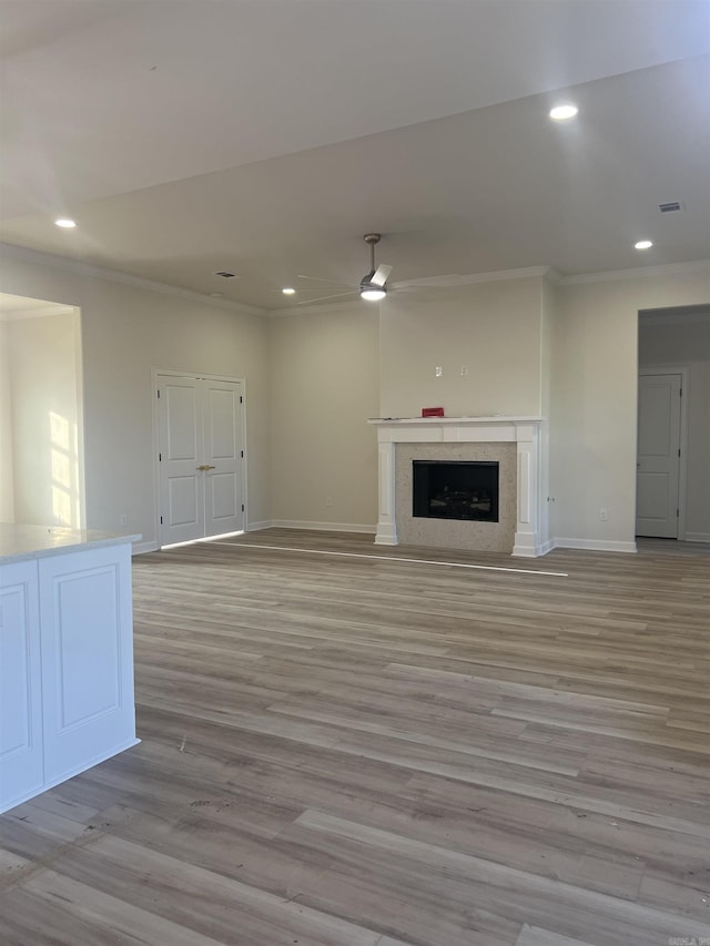 unfurnished living room featuring recessed lighting, a fireplace, light wood-style flooring, baseboards, and ornamental molding