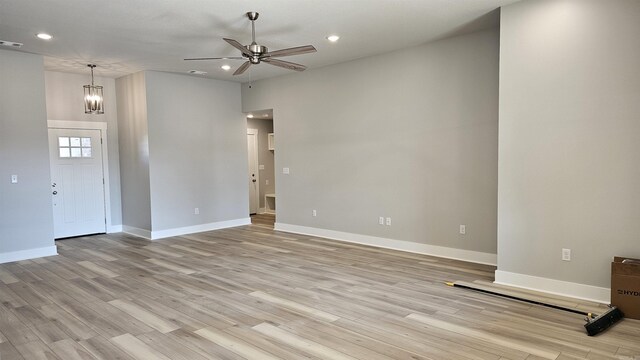 unfurnished living room with light wood-type flooring, ceiling fan with notable chandelier, baseboards, and recessed lighting