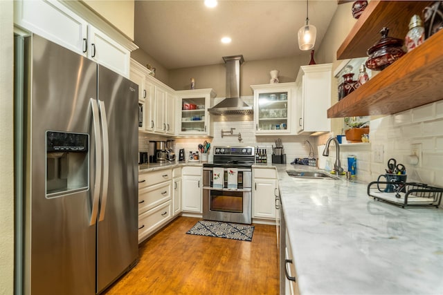 kitchen with appliances with stainless steel finishes, wall chimney exhaust hood, sink, decorative light fixtures, and white cabinetry