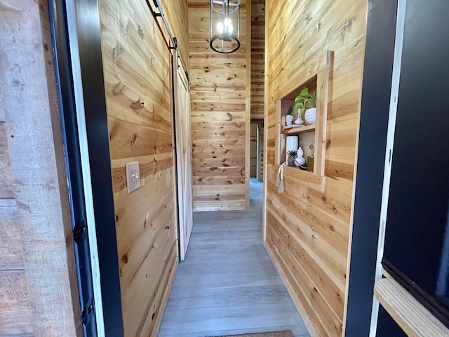 corridor with a barn door, hardwood / wood-style flooring, and wood walls