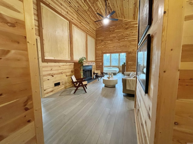 living area with wooden ceiling, high vaulted ceiling, wooden walls, ceiling fan, and light hardwood / wood-style floors