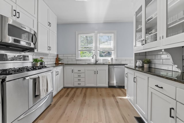 kitchen with sink, stainless steel appliances, light hardwood / wood-style flooring, dark stone counters, and white cabinets