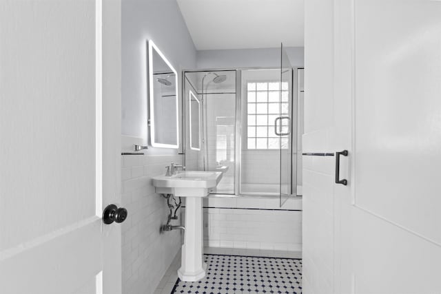 bathroom featuring sink, bath / shower combo with glass door, and tile walls