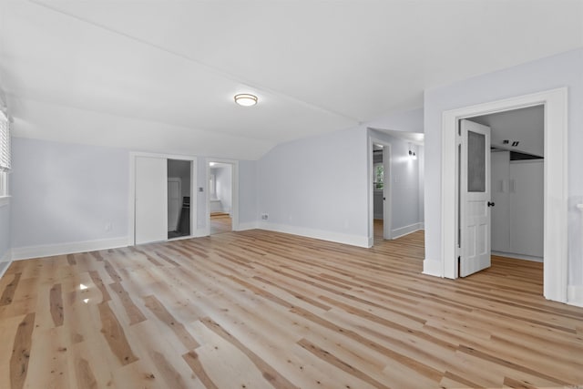 unfurnished bedroom featuring ensuite bath, a closet, lofted ceiling, and light hardwood / wood-style flooring