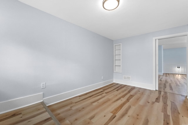 unfurnished room with built in shelves and light hardwood / wood-style floors