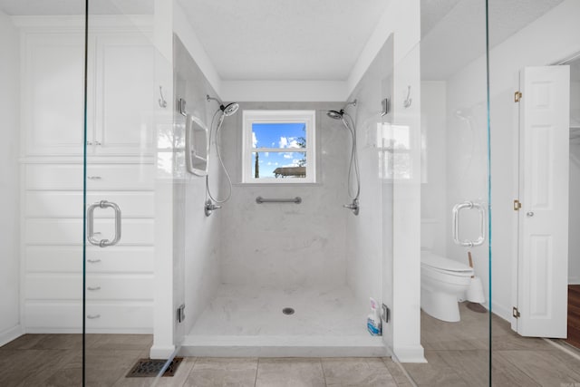 bathroom with a textured ceiling, toilet, and a shower with door