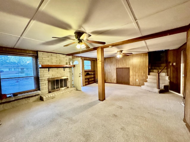 basement featuring ceiling fan, light colored carpet, a brick fireplace, and wood walls