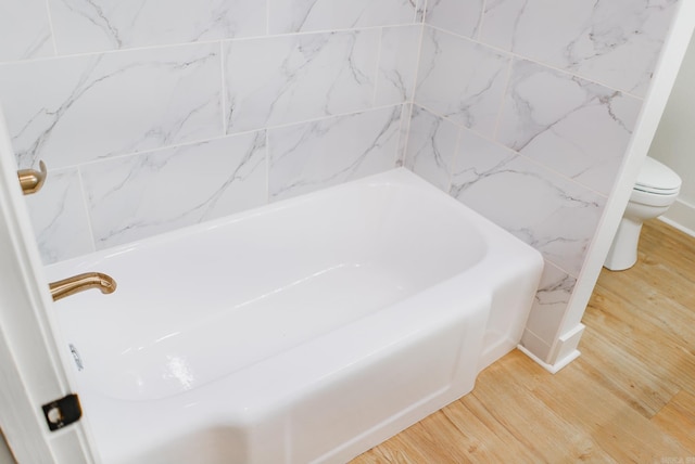 bathroom with a tub to relax in, toilet, and hardwood / wood-style flooring