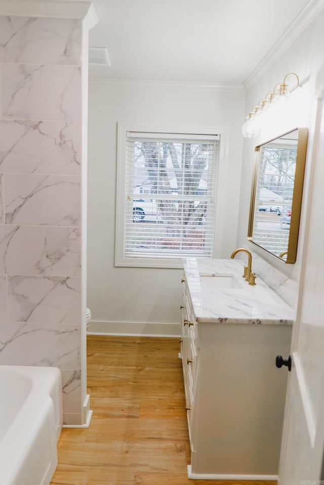 bathroom featuring a washtub, wood-type flooring, vanity, and ornamental molding