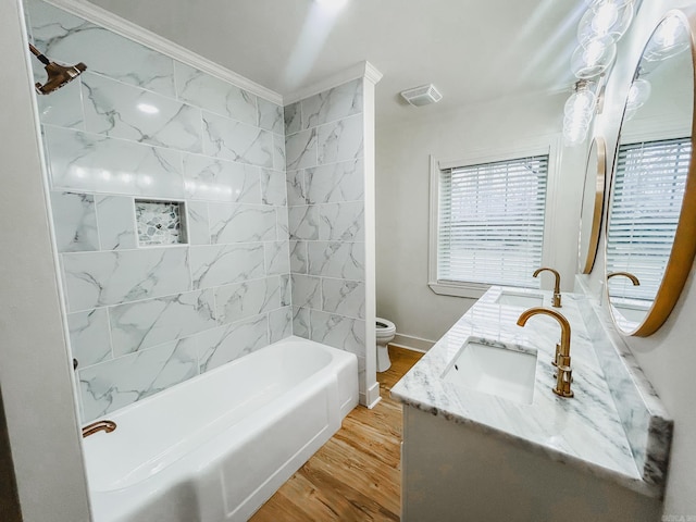 full bathroom with ornamental molding, vanity, tiled shower / bath combo, hardwood / wood-style flooring, and toilet