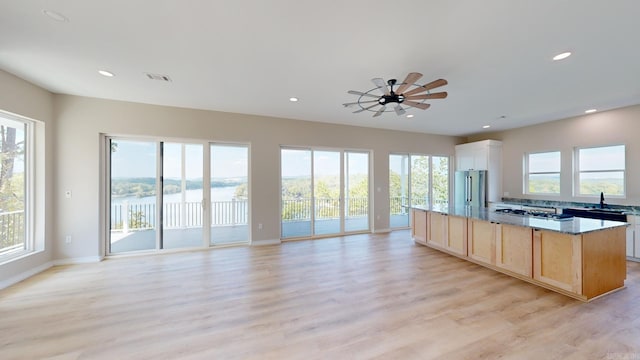 kitchen with ceiling fan, light stone countertops, stainless steel appliances, light brown cabinetry, and light wood-type flooring