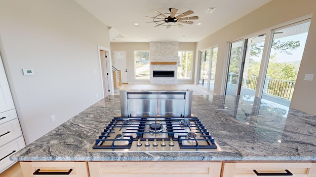 kitchen featuring stone counters, ceiling fan, stainless steel gas cooktop, a fireplace, and light brown cabinetry