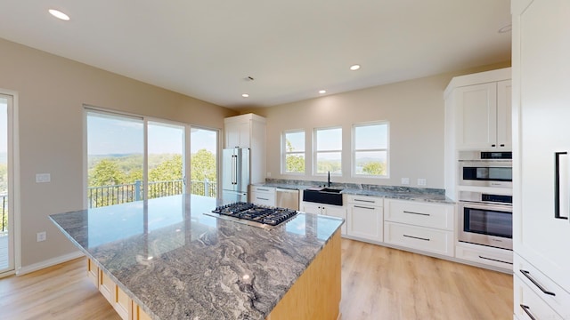 kitchen with light stone countertops, a center island, white cabinets, and appliances with stainless steel finishes