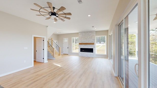 unfurnished living room featuring a stone fireplace, ceiling fan, and light hardwood / wood-style flooring