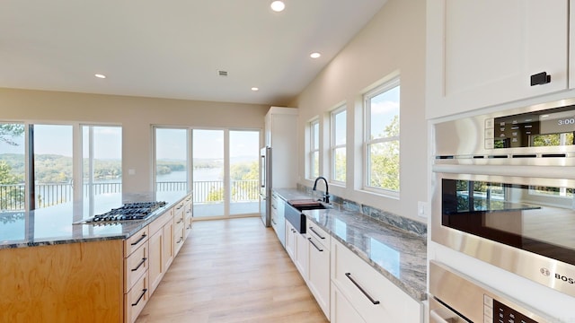 kitchen with sink, stainless steel appliances, light stone counters, plenty of natural light, and white cabinets