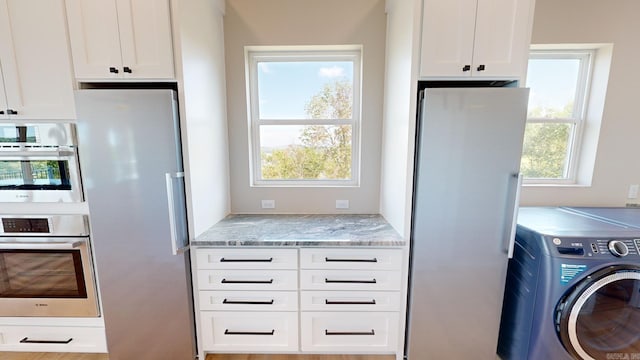 kitchen featuring white cabinets, stainless steel fridge, washer / dryer, and light stone countertops