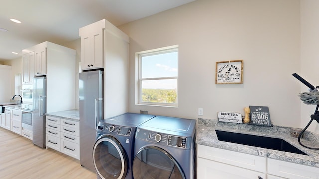 washroom featuring cabinets, light wood-type flooring, sink, and washing machine and clothes dryer